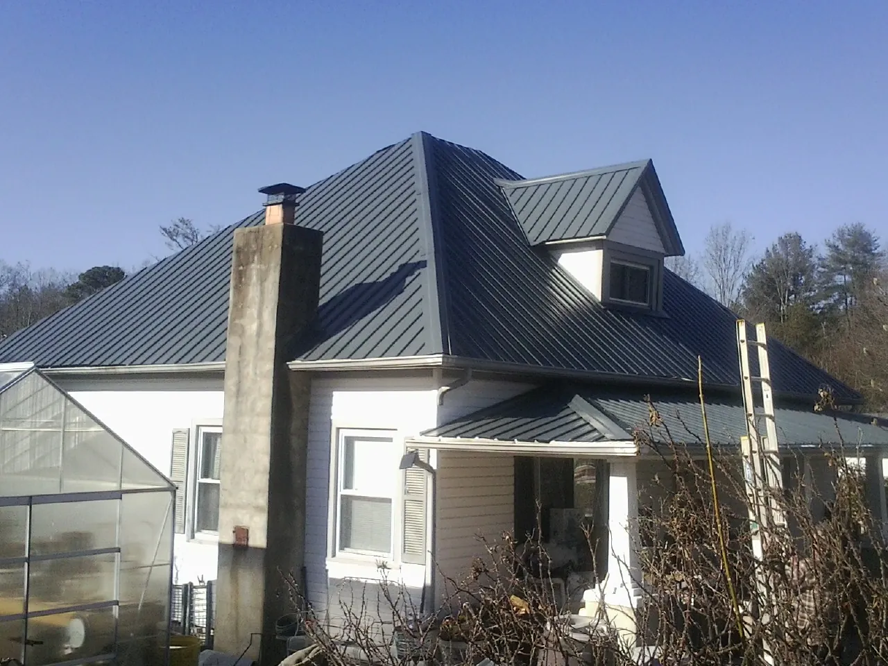 Dark blue standing seam metal roof on a white farmhouse with dormer — Slate & Tile Roof Repair by Roofing Brothers in Lavina