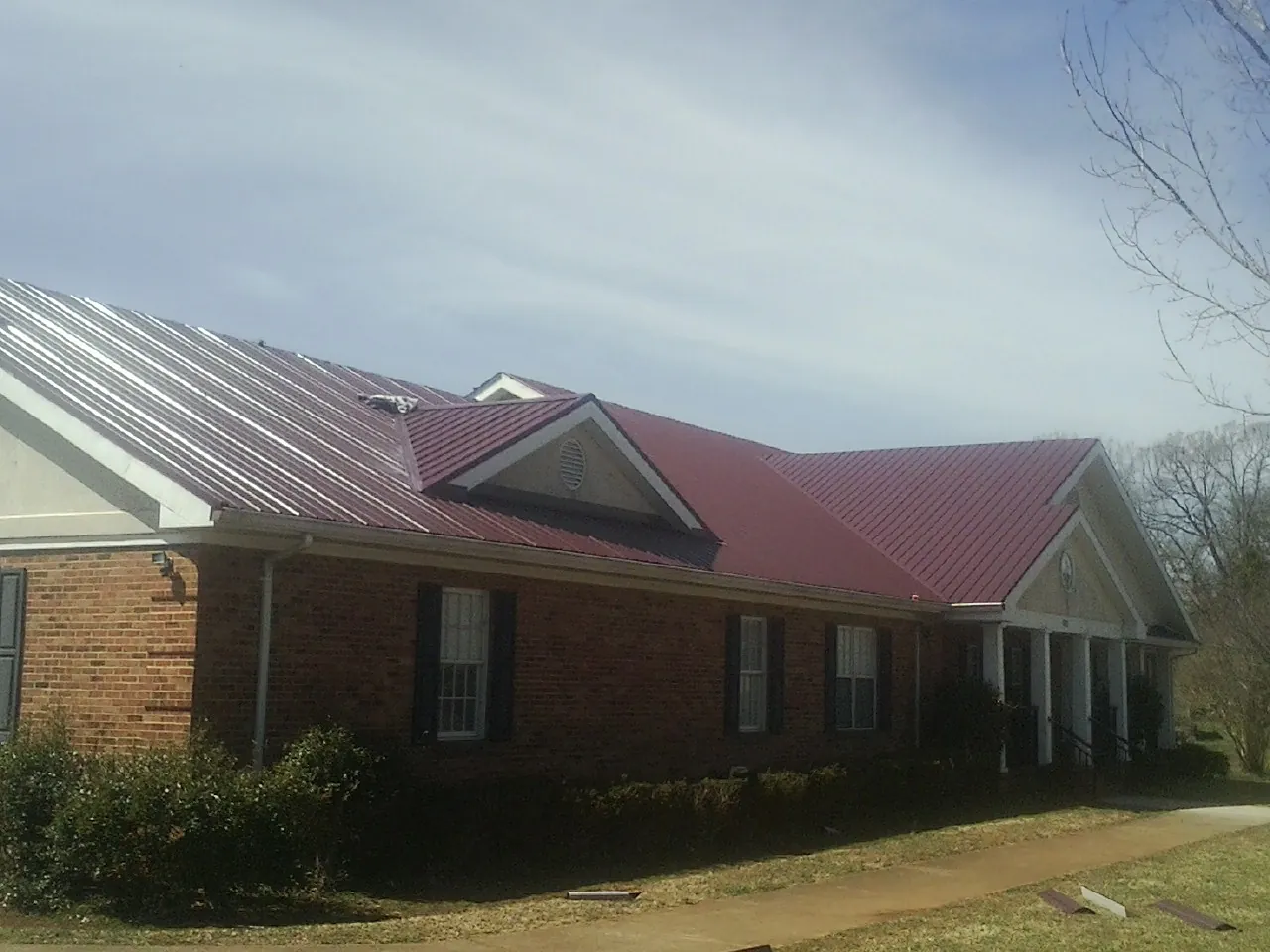 Red metal roof with gabled entries on a long brick building, from a Hail Damage Roof Repair job in Lavina