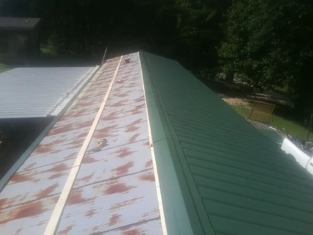 Old rusted panels beside newly installed green metal roofing — Wind Damage Roof Repair by Roofing Brothers in Lavina
