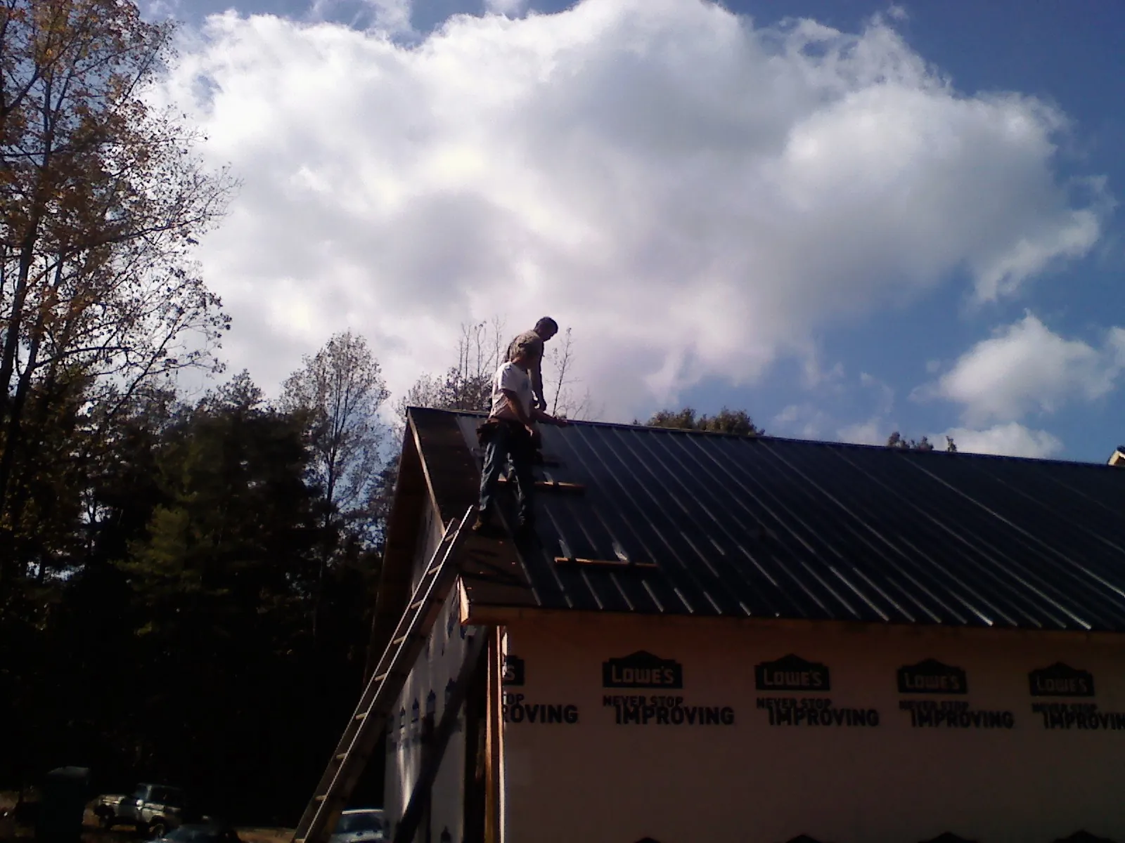 Roofer fastening dark metal panels high against a cloudy sky, from a Roof Inspection job in Lavina