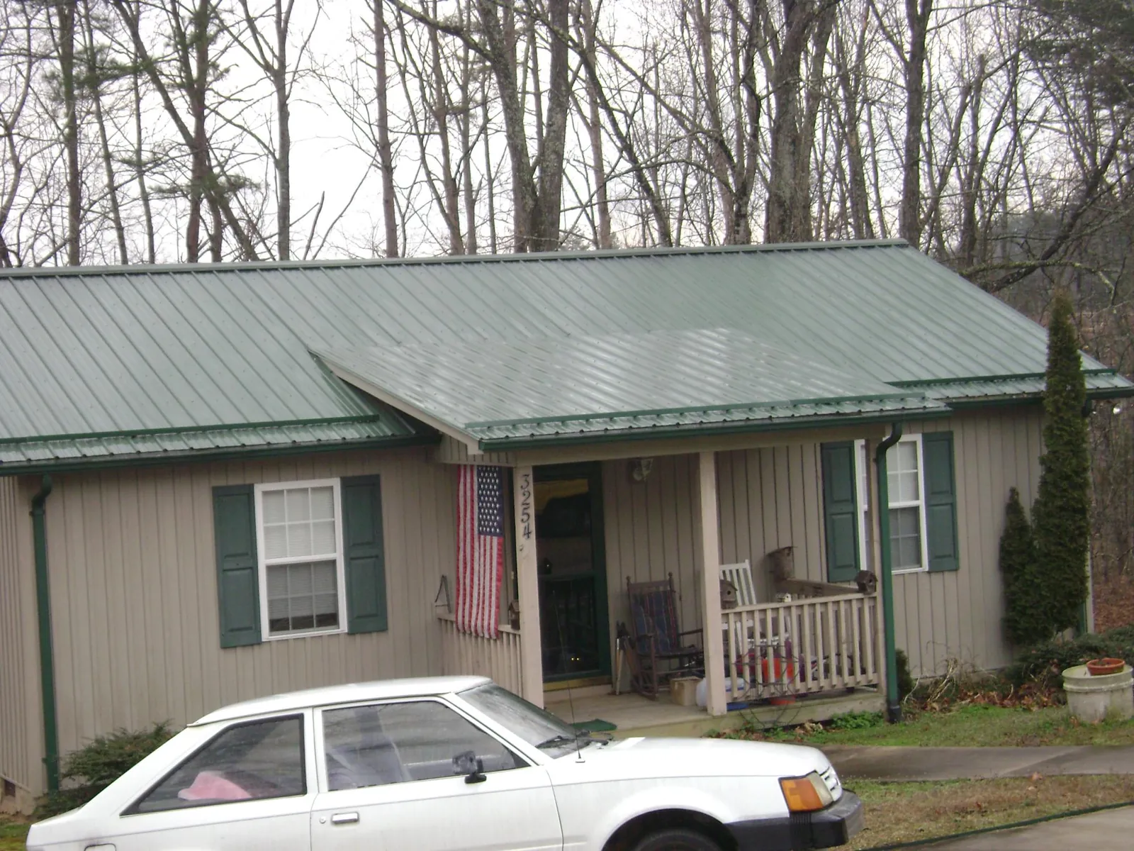 Green metal roof and front porch on a tan sided cottage in Lavina